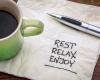 Kaffeebecher, Stift und weiße Serviette auf der steht: Rest, Relax, Enjoy - so geht es entspannt zum Wohlfuehlgewicht